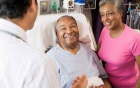 Man lying in hospital bed with woman at his side; both speaking with a physician.
